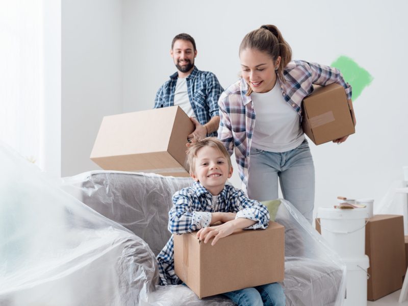Young family relocating and renovating their new house, they are carrying boxes, boy smiling on the foreground